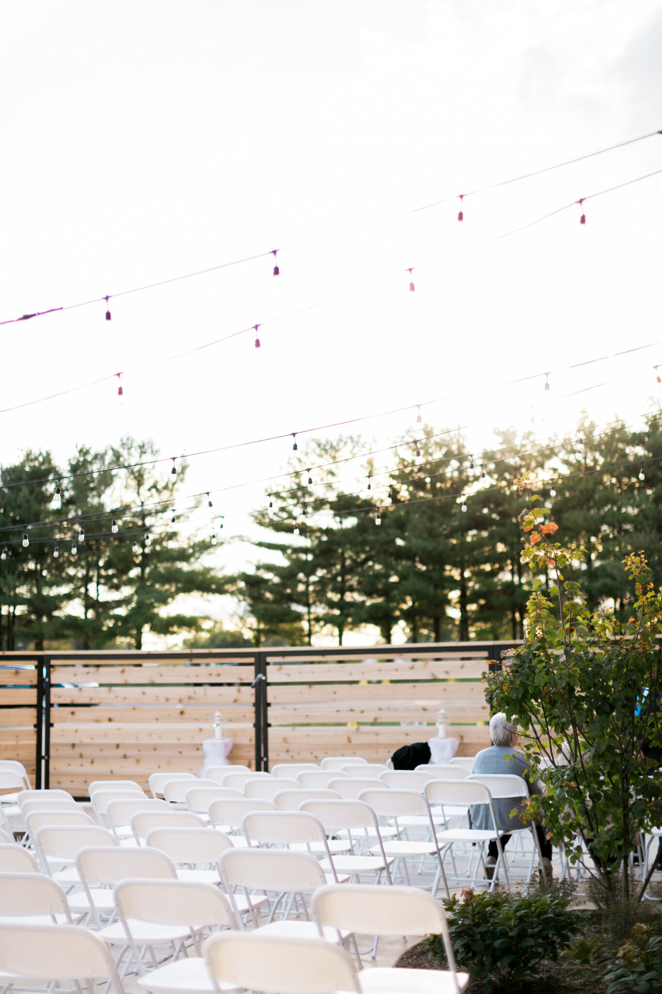 Woman sitting alone in a sea of foldable white chairs inside a fenced open area